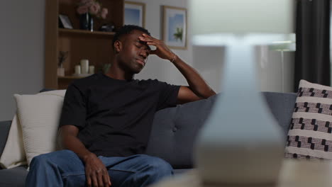 unhappy and depressed young man sitting on sofa at home looking anxious and worried resting head on hand 4