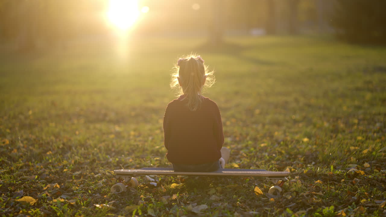 Girl sitting on a skateboard in a park at sunset