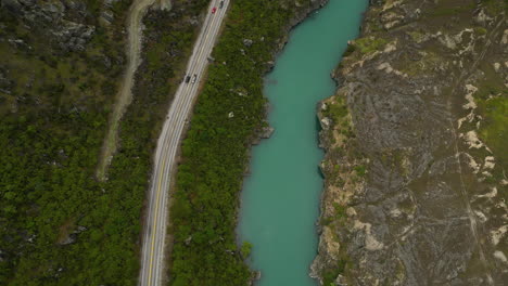 aerial top down view of a forest road and where vehicles pass next to a turquoise river in a beautiful valley