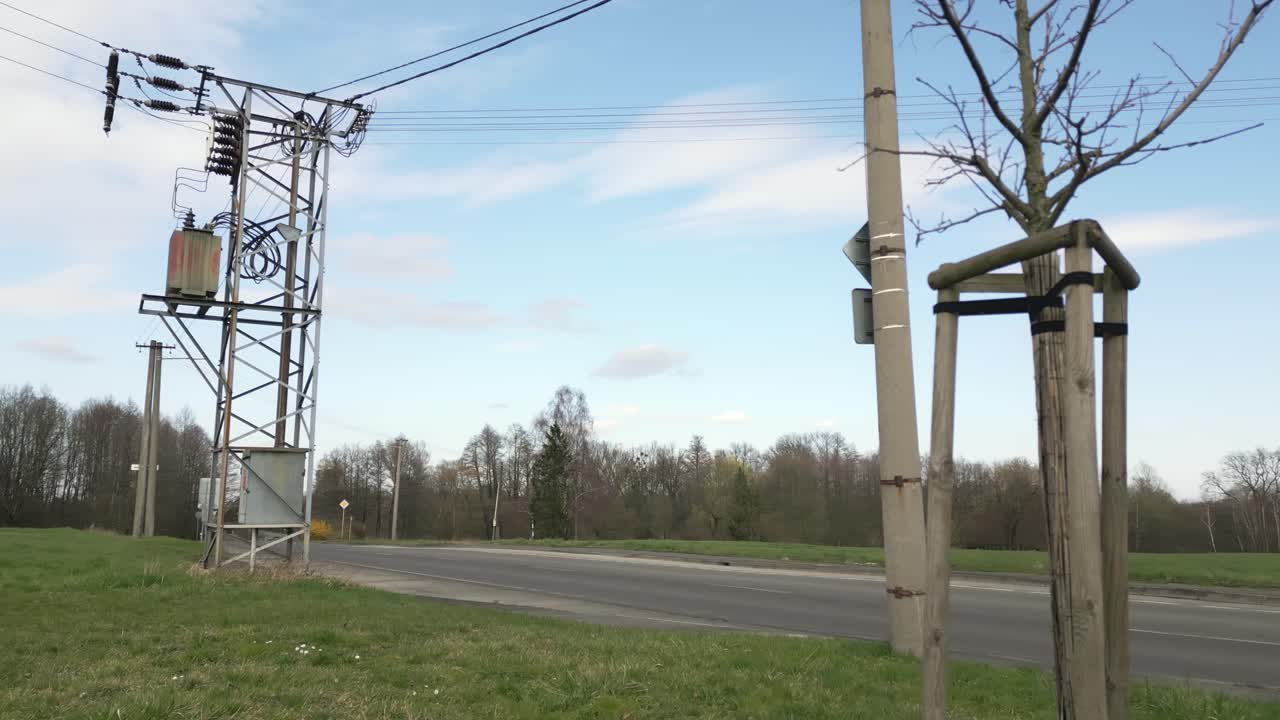escena al aire libre serena con equipos eléctricos, un árbol desnudo y una carretera bajo un cielo despejado
