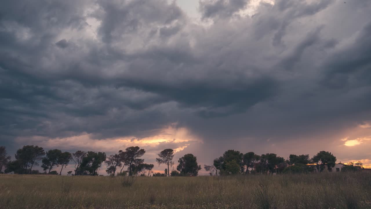 Dramatiske, stormfulde himmelstrøg med skyer og gyldent lys under solnedgang med en trærække i forgrunden