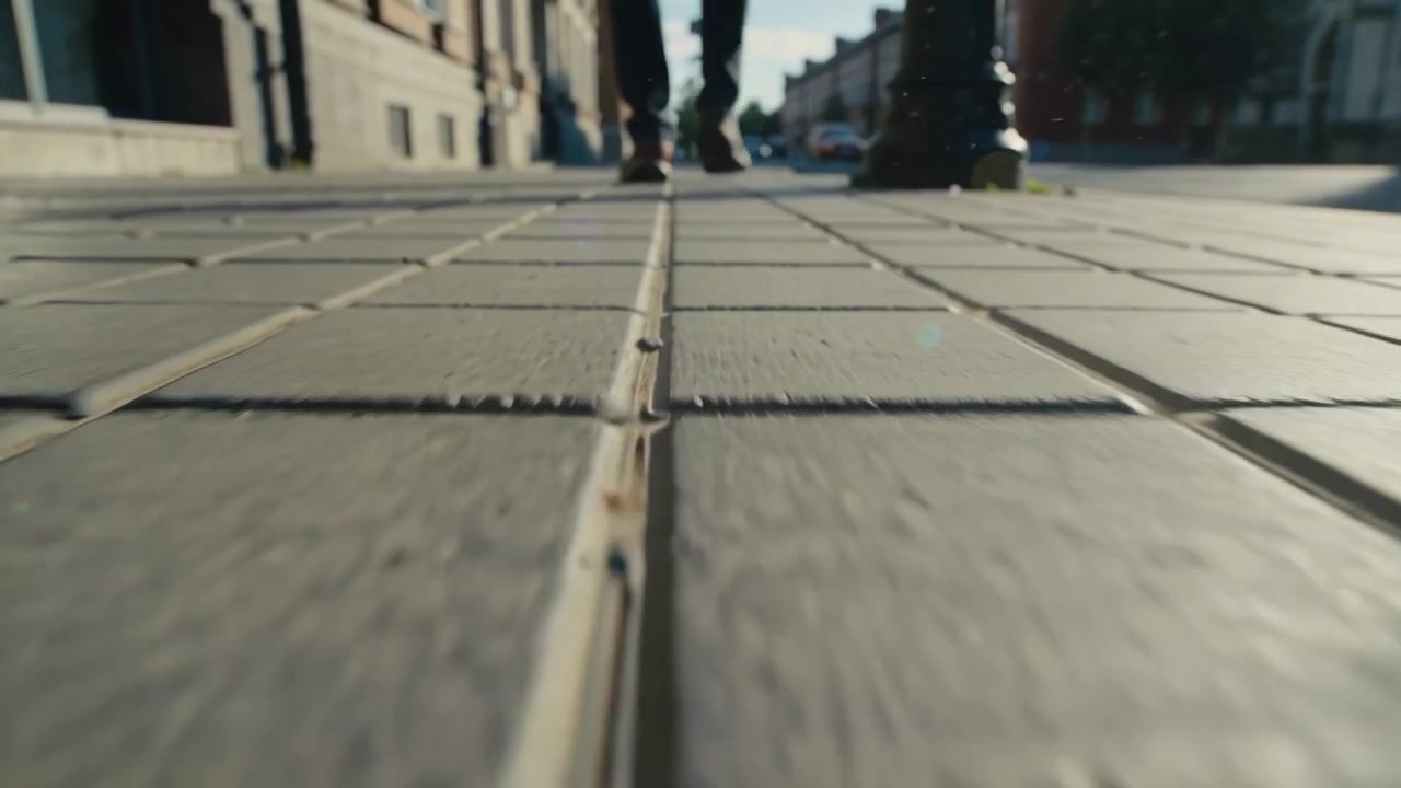 Walking man wearing dark trousers and shoes approaching low camera on tiled sidewalk, lamppost
