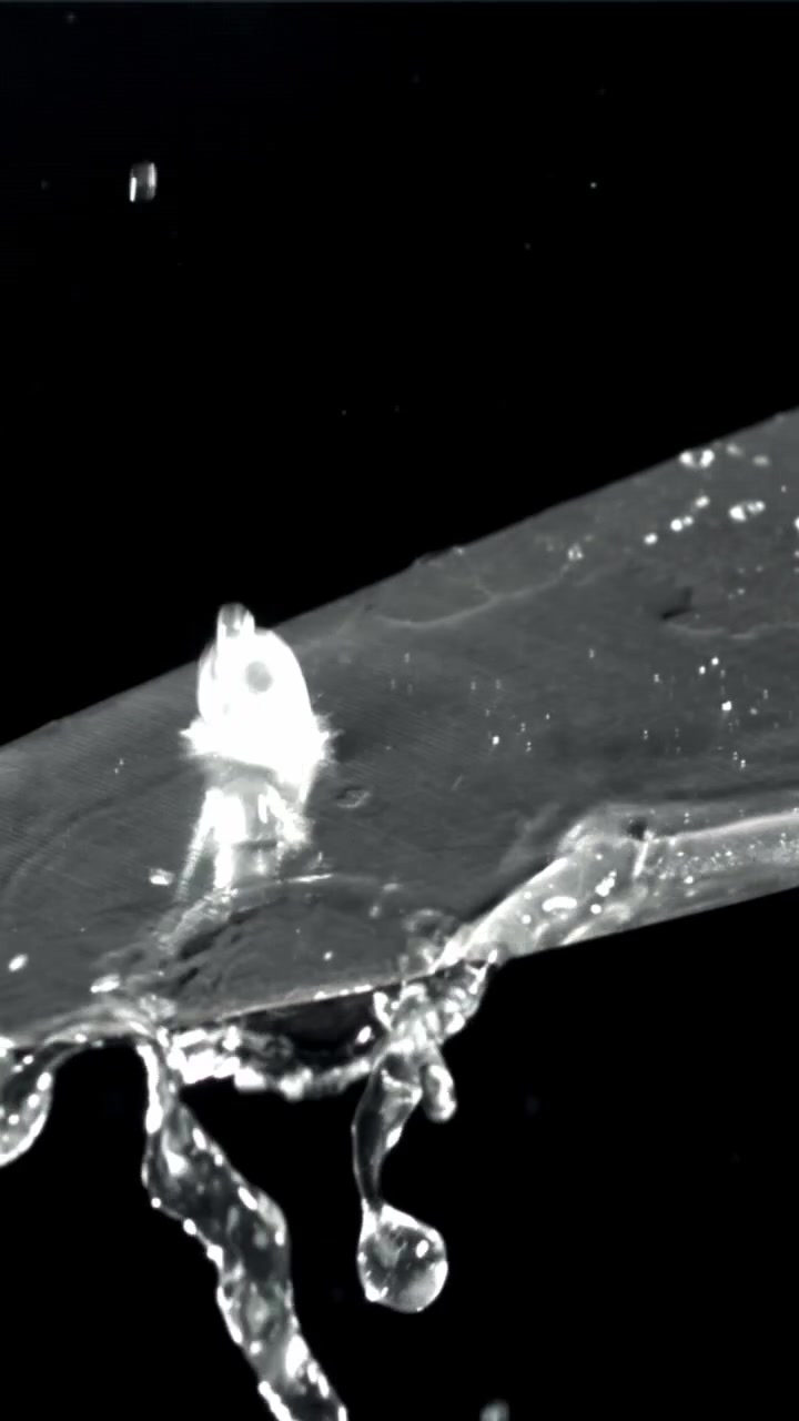 Goccioline d'acqua al rallentatore che schizzano e gocciolano su una lama di coltello metallica