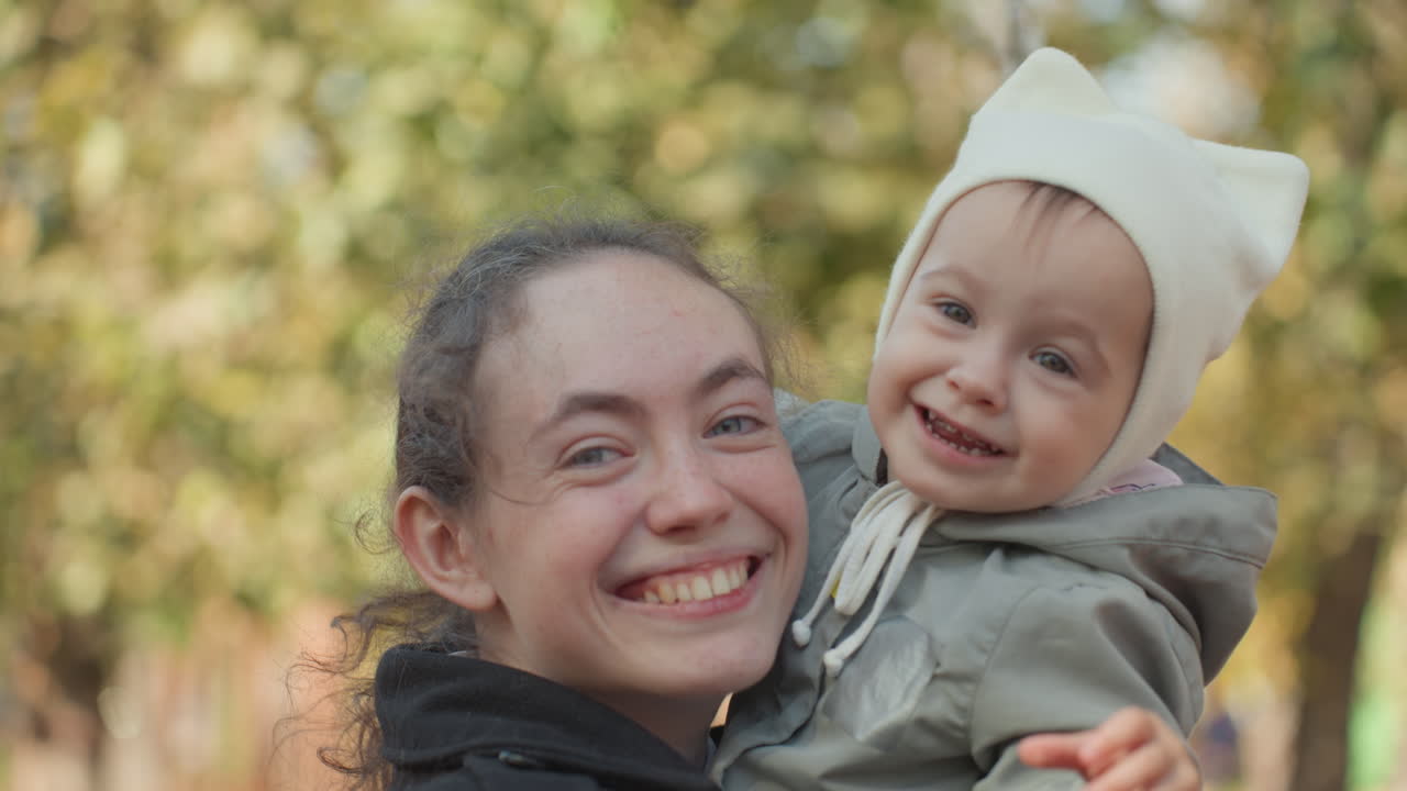 Family hugs outdoors. Mother comforts smiling child outdoors. Mother embraces joyful kid among bright leaves. Joyful family scene with mother embracing happy child outside among trees