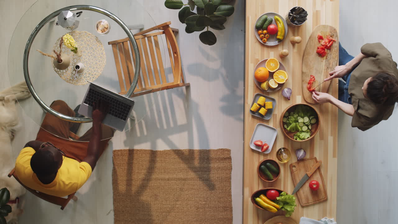 la esposa cocinando ensalada y el marido usando una computadora portátil en casa