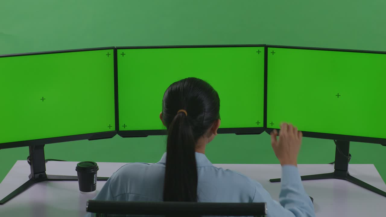 녹색 스크린 스튜디오에서 모의 여러 컴퓨터 모니터와 함께 작업하는 동안 잠자리에 들기 전에 는 피곤한 아시아 여성의 뒷면