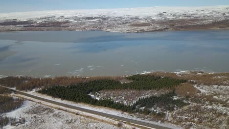 Aerial-view-moving-in-on-a-beautiful-Icelandic-lake-surrounded-in-snow-spotted-lands