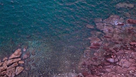 Overhead-view-of-small-paradisiac-bay,-tilt-reveals-offshore-lighthouse,-dusk