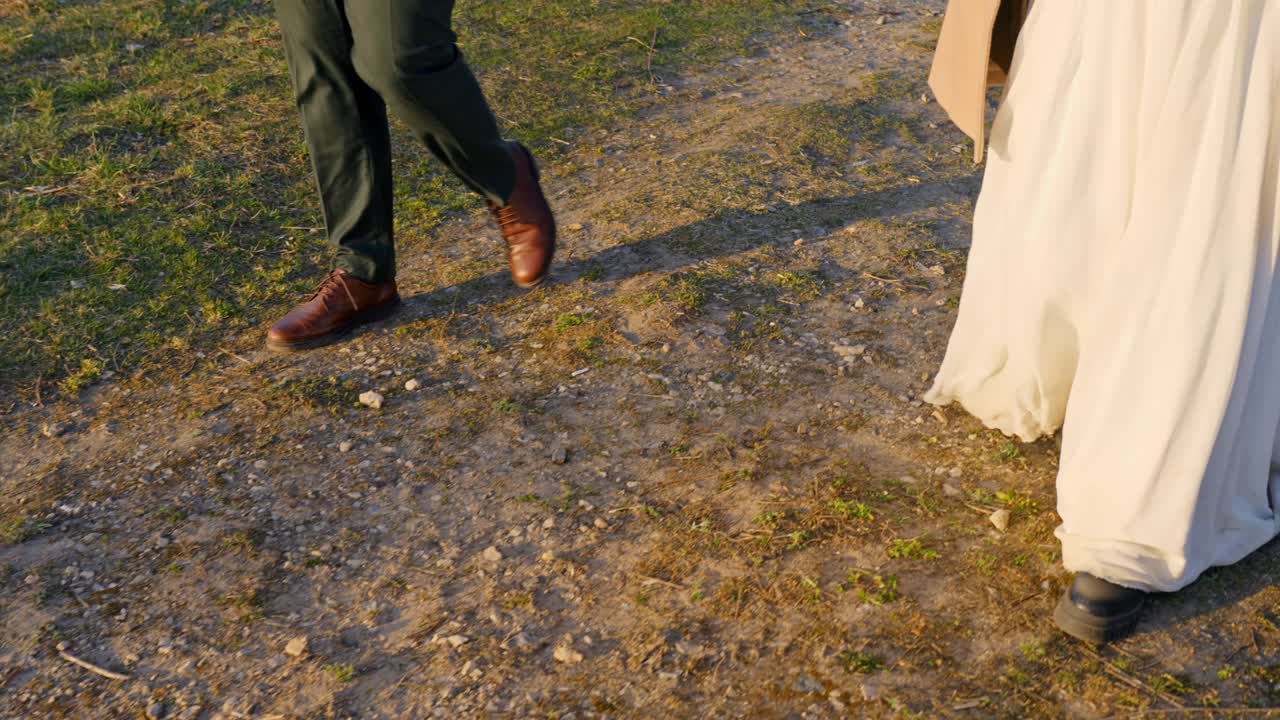 Walking together on a sunset-lit path, a couple moves in formal attire, a wedding moment