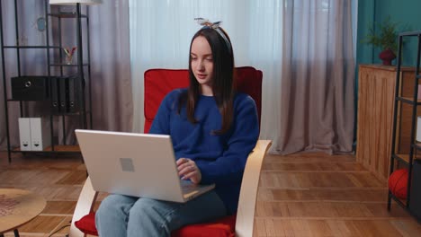 mujer joven caucásica sentada en el sofá abriendo una computadora portátil comenzando a trabajar en línea en la sala de estar en casa