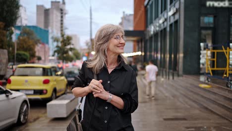 happy mature woman with glasses and gray hair walks smiling along the city street. walking from work or on a date