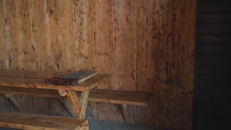 wooden resort seating area features l shaped wooden benches and table with skewers neatly arranged on top, set against textured wood-paneled walls and stone floor