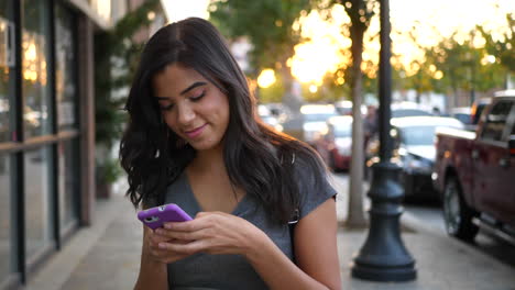una mujer hispana caminando por las calles de la ciudad enviando mensajes de texto y luciendo feliz con un mensaje en su teléfono celular a cámara lenta