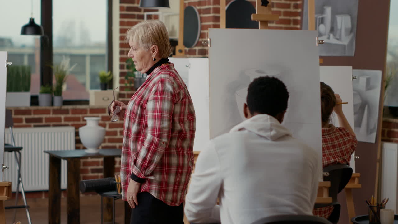 Artist supervising senior man drawing on canvas in art class