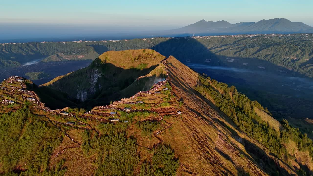 Drone footage captures Mount Batur Vulcan in Bali, Indonesia, with hikers gathered on the volcanic summit overlooking the sunrise and the surrounding tropical forest and sea