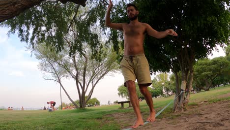 Hispanic-man-balances-on-slack-line-in-park,-slow-motion