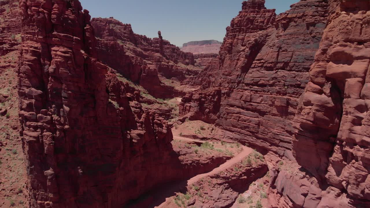 Vista aerea: Pareti di canyon rosso intenso con una stretta strada sterrata vicino a Moab, Utah