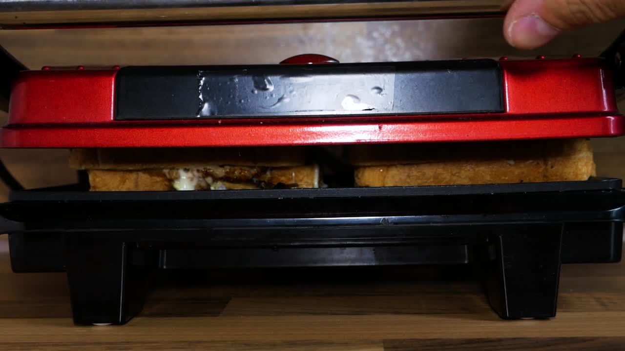 Opening sandwich cooking machine and preparing to take out steaming hot, delicious sandwiches for dinner.