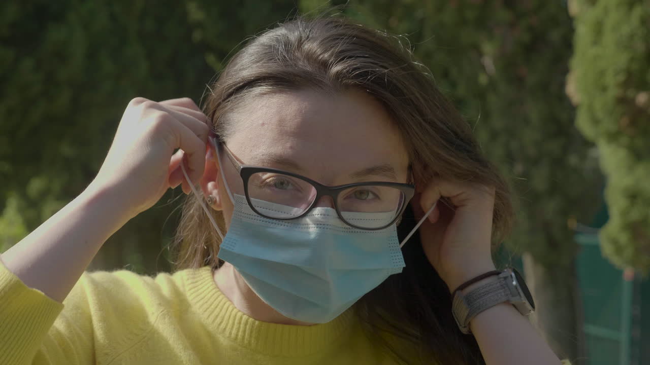 Ripresa al rallentatore di una giovane donna millennial caucasica con occhiali che indossa la sua mascherina protettiva.