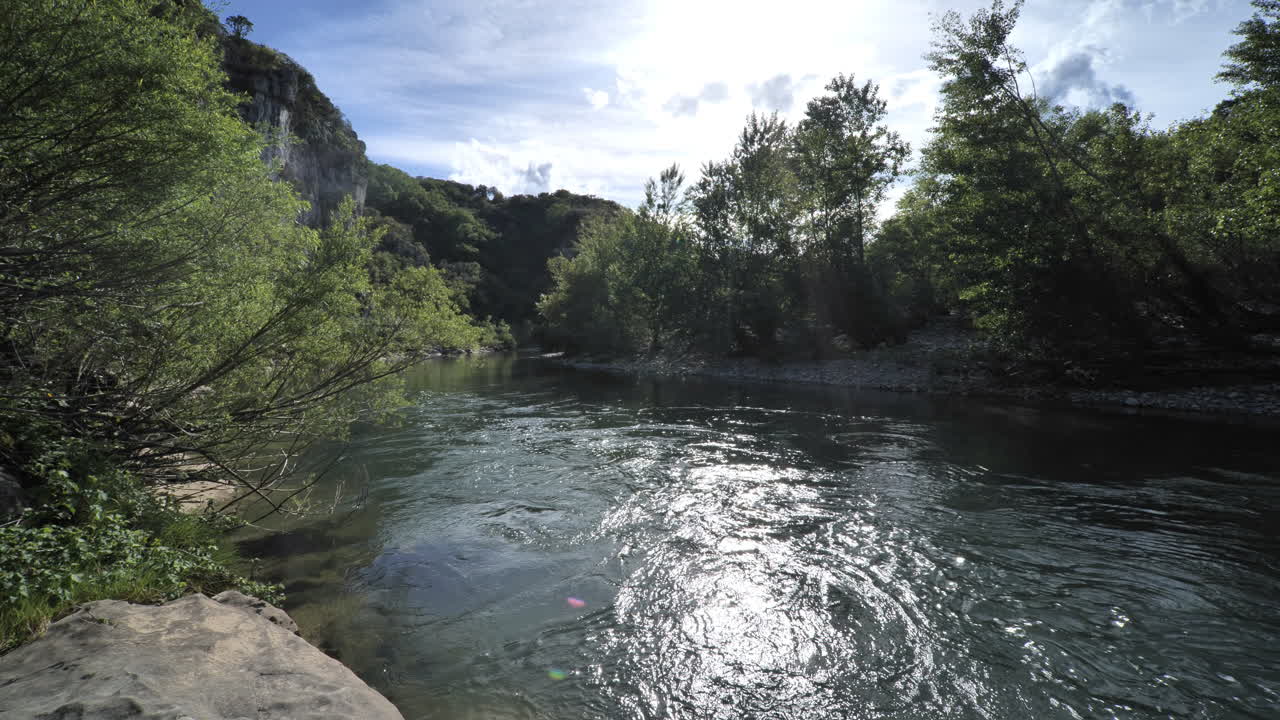 Inquadratura statica di un fiume che scorre in una foresta lungo scogliere, Francia.