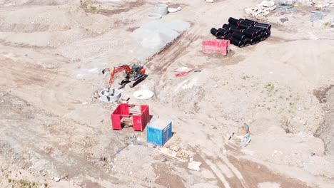 excavation digger vehicle preparing concrete pipe aerial view on housing development construction site slow tilt down flyover