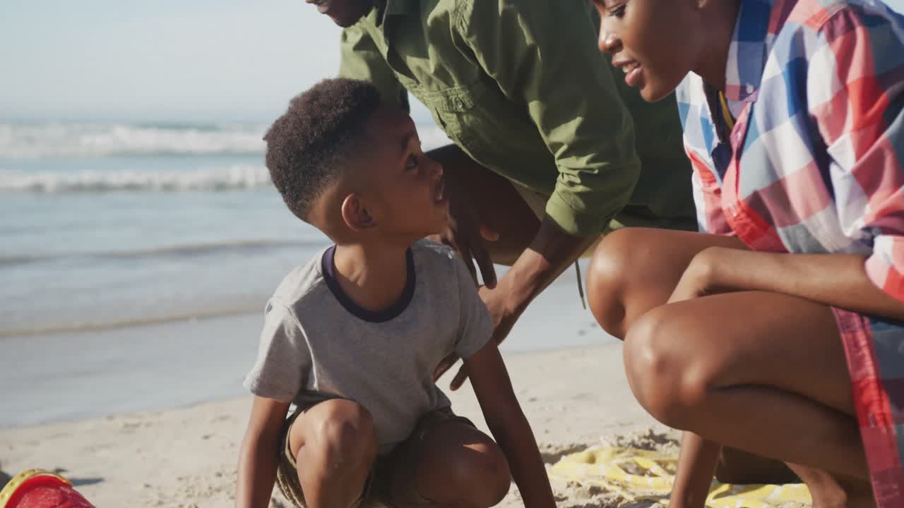 Afroamerikansk par, der leger med deres søn i sandet på stranden.
