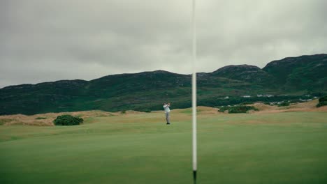 male golfer hits chip shot onto putting green on ireland links golf course, ball bounces in slow motion and rolls away from pin