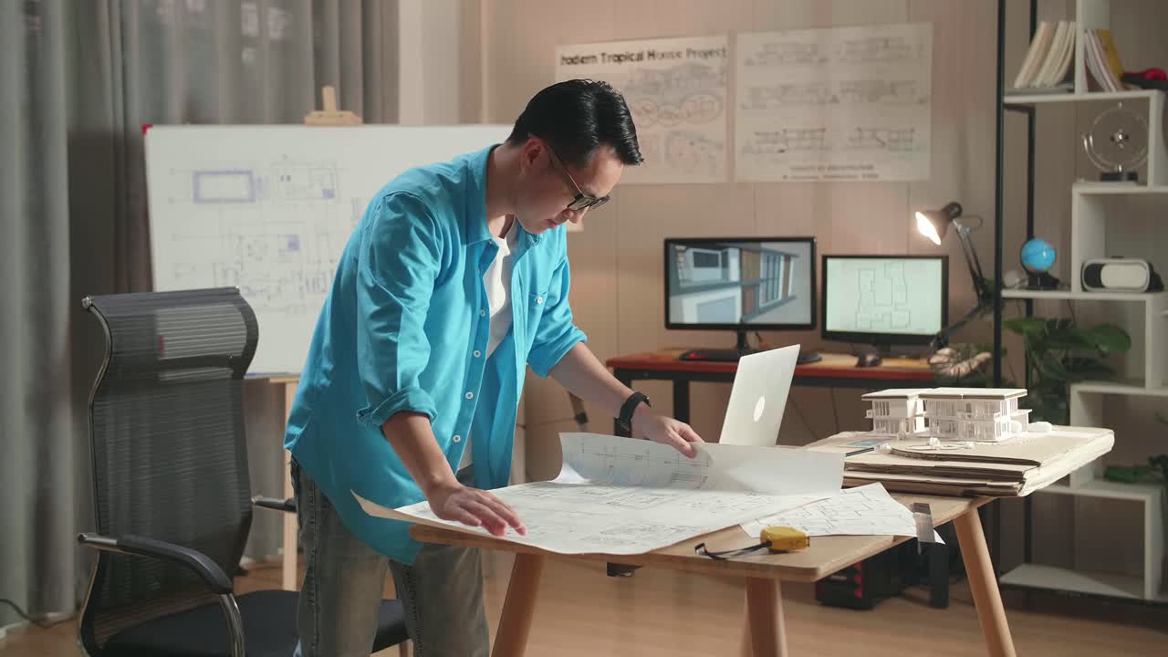 Asian Man Engineer With A Laptop Looking At Blueprint While Working At The Office