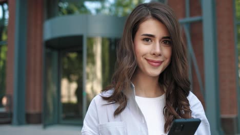 caucasian student woman using smartphone in the street and looking at camera