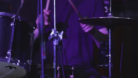drummer playing full kit under stage lights mid-performance in live concert.