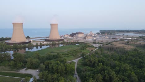 nuclear power plant chimneys with rising smokes on lake coastline, aerial view