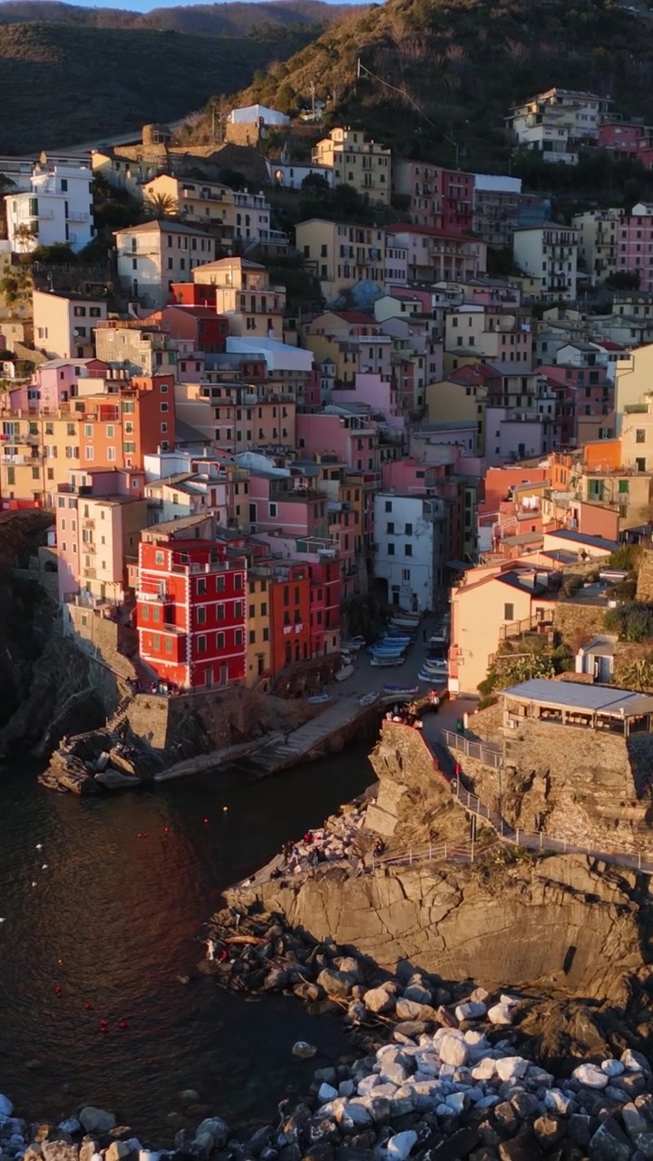 Vue aérienne par drone en recul du village de Riomaggiore à flanc de falaise, du pont-viaduc et de la côte rocheuse au coucher du soleil, Cinque Terre, Italie.