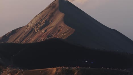 drone shot tilting away from hikers in front of a smoking volcano in guatemala