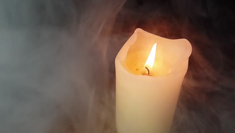 haunted theme and scary white smoke fog rolling over an old oak table with a dark background over and past a burning candle flame