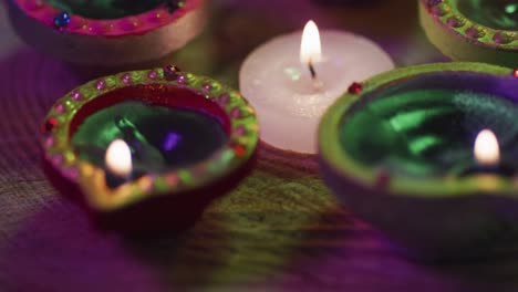 Lit-candles-in-decorative-clay-pots-and-tea-light-candle-on-wooden-table-top,-bokeh-background