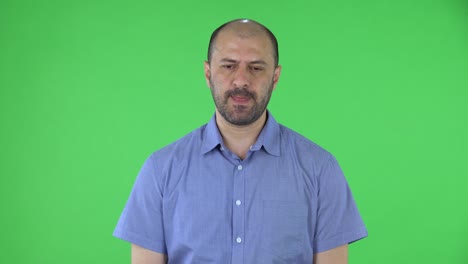 retrato de un hombre de mediana edad mirando a la cámara con emoción y emoción. hombre calvo con barba en camisa azul posando en pantalla verde en el estudio.