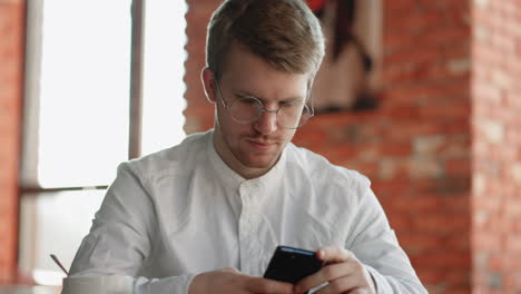 Un-Hombre-Atractivo-Con-Gafas-De-Pie-Solo-En-El-Interior-Sosteniendo-En-Las-Manos-El-Número-De-Marcación-Del-Teléfono-Inteligente-En-La-Pantalla-Táctil.-Mujer-Joven-Y-Alegre-Navegando-Por-Internet,-Navegando-Por-Internet,-Elige-El-Concepto-De-Compra-De-Productos-En-Línea