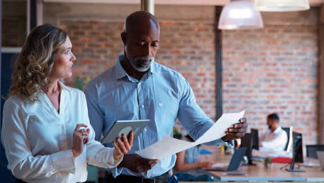 Male-And-Female-Business-Colleagues-With-Digital-Tablet-And-Documents-Meeting-In-Busy-Office