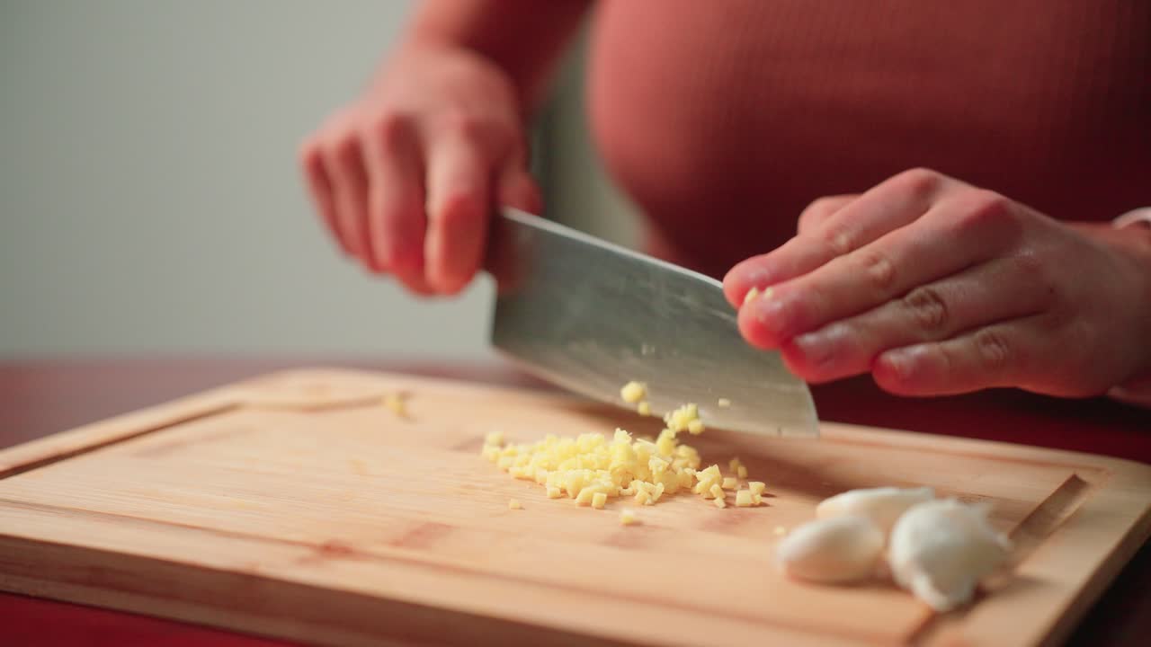 Woman mincing ginger by hand with a knife on a cutting board