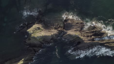 aerial footage over a rocky island with waves crashing on it