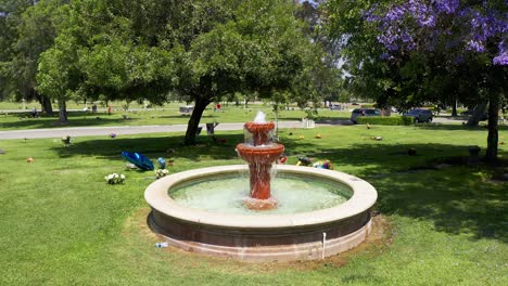 Aerial-descending-close-up-shot-of-a-decorative-fountain-amidst-flowered-grave-sites-at-a-California-mortuary