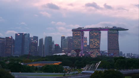 Day-to-night-time-lapse-shot-at-marina-barrage-rooftop-park-overlooking-at-Supertree-grove-in-Gardens-by-the-bay-and-downtown-cityscape-featuring-landmark-Marina-Bay-Sands-against-fast-moving-clouds