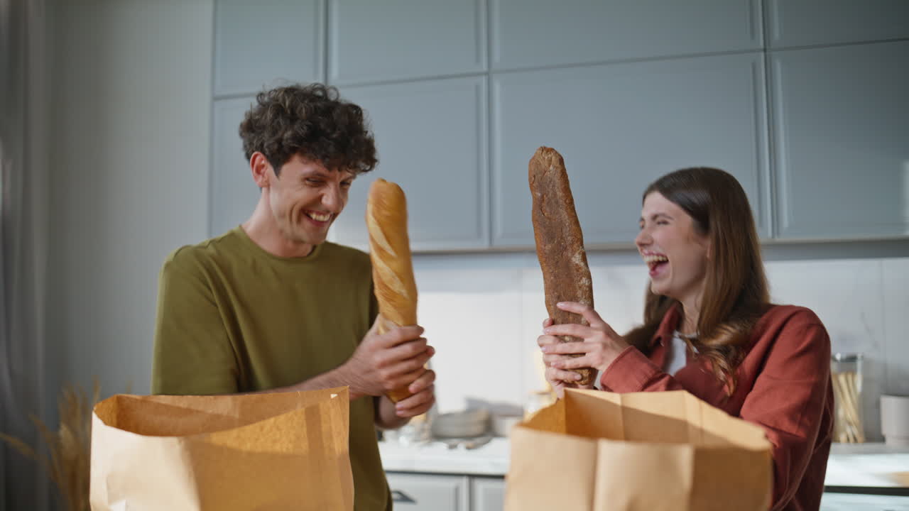 Funny couple fighting baguettes house kitchen closeup. Family unpacking products