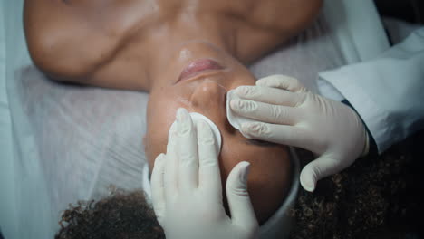 close-up cosmeticus zette katoenen pads op de ogen. top view vrouw liggende kliniek bank