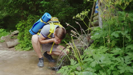 viajero cansado con una mochila bebe agua de un manantial en el bosque hd video