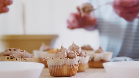 close up of young downs syndrome couple decorating homemade cupcakes with icing in kitchen at home