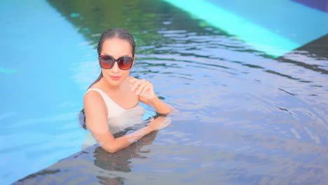 Hermosa-Y-Sexy-Mujer-Exótica-Con-Gafas-De-Sol-En-El-Agua-De-La-Piscina-En-Vacaciones-Tropicales-De-Lujo,-Cámara-Lenta