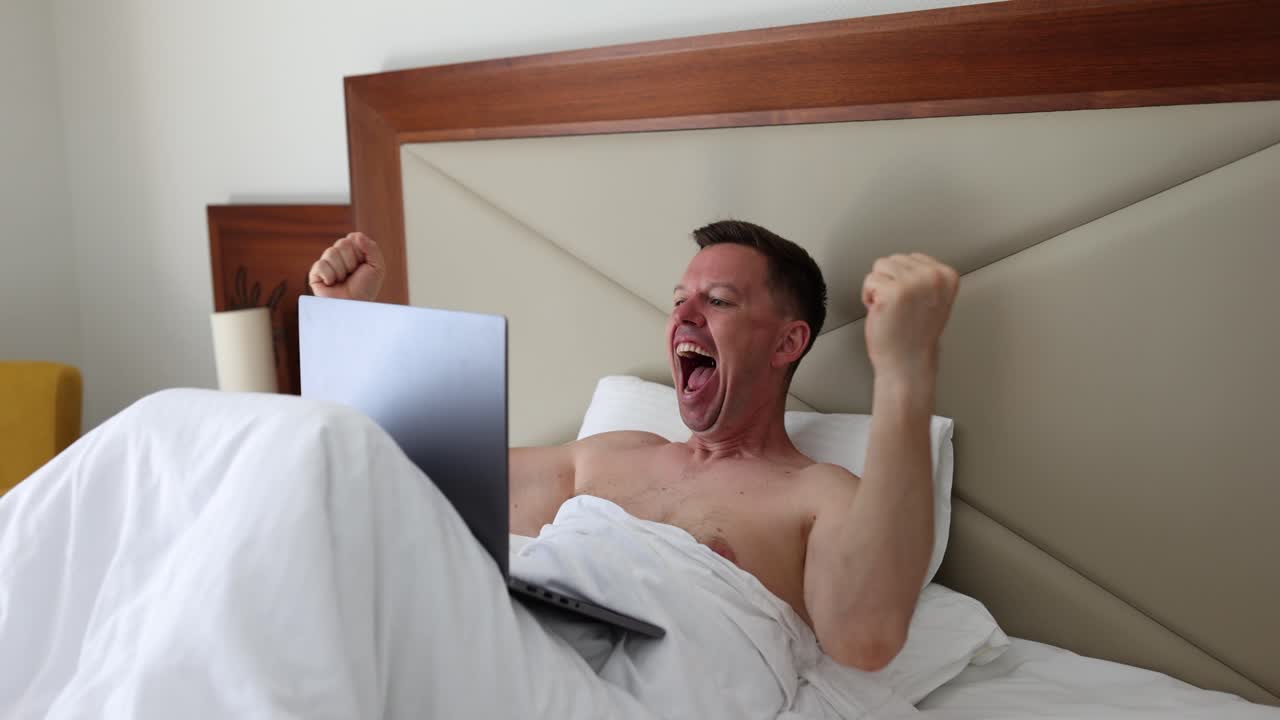 Excited man celebrating success with laptop in bed