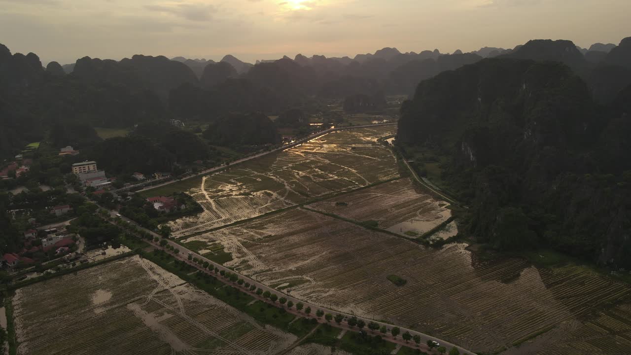 High drone view of Ninh Binh, Vietnam, with rice fields, karst mountains, and farm village during cloudy golden sunset