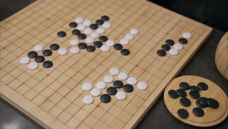 overhead 45 degree view of man's hand placing a white stone in the middle of the ancient chinese board game go on a bamboo wooden board with black pieces scattered in the foreground